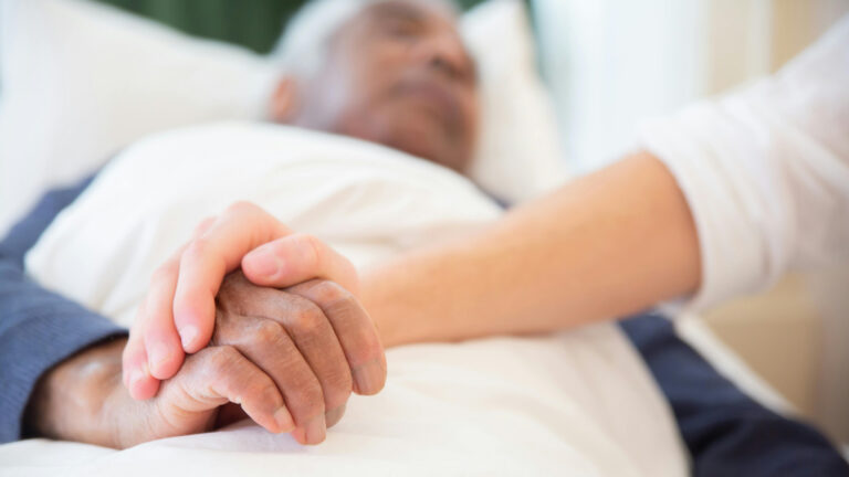 Young person's hand holding an old person's hand in hospital